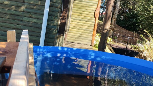 A wooden deck with a blue pool, a white pipe, and a wooden door.