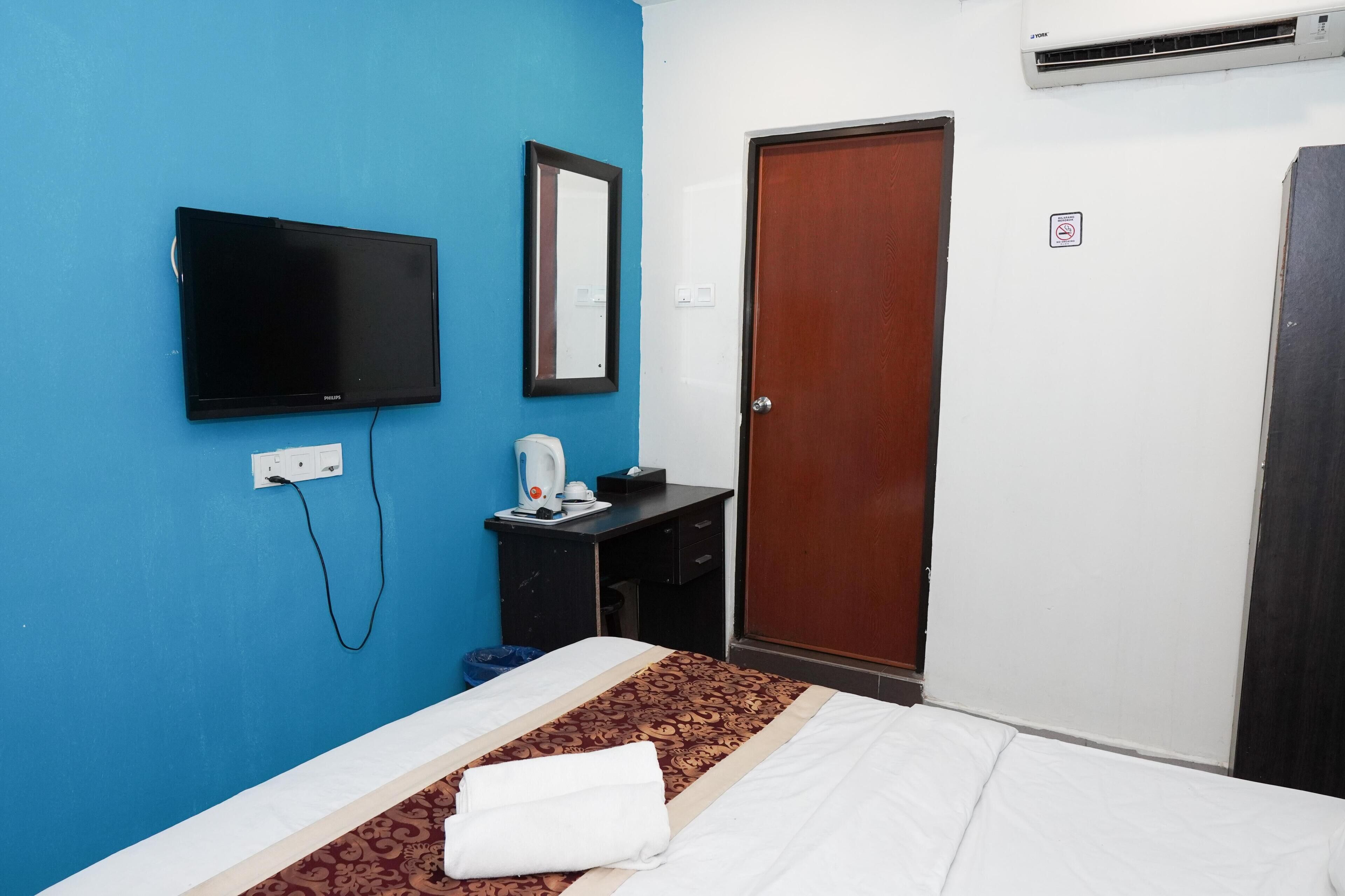 Habitación de hotel con cama, escritorio con hervidor, televisor de pantalla plana, espejo y puerta.