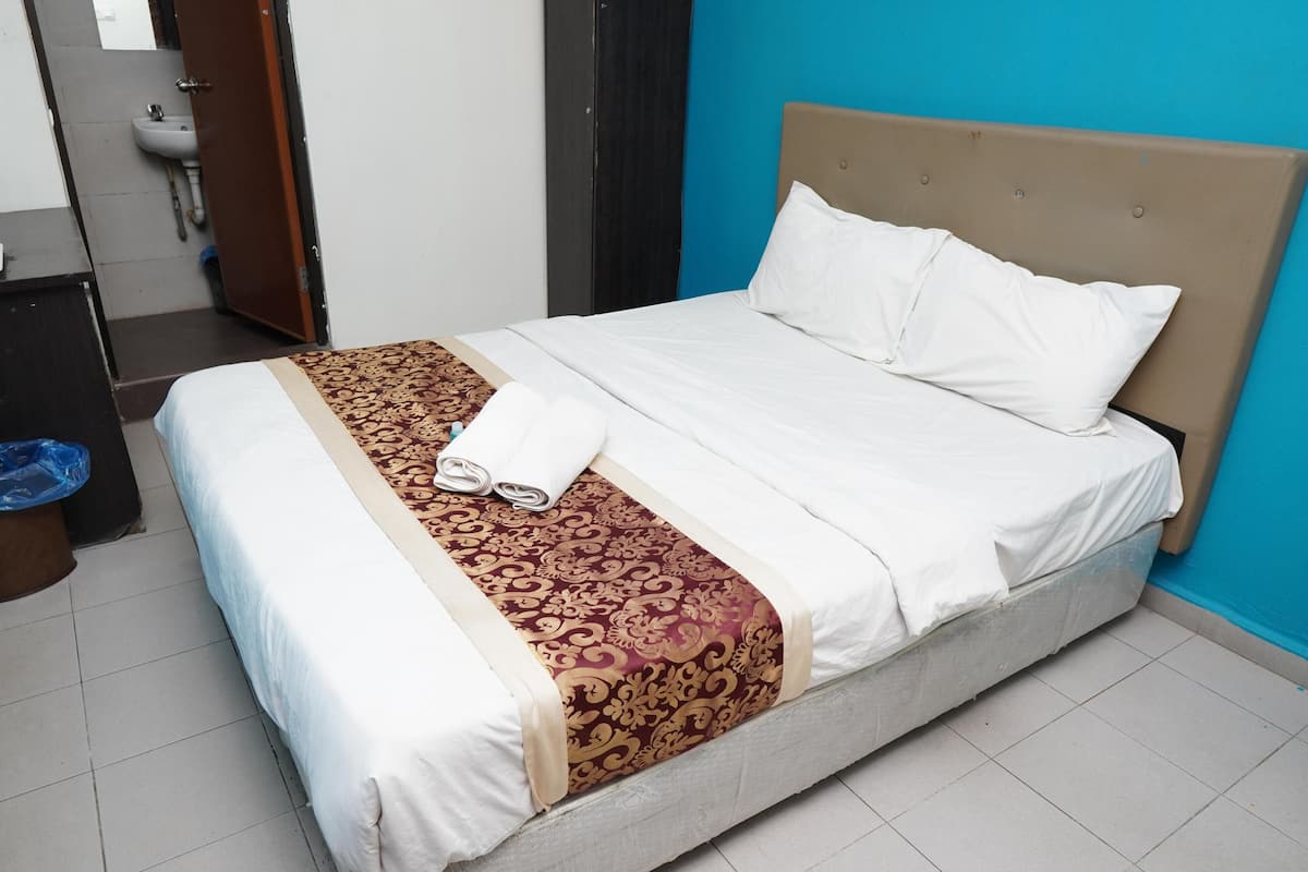 Een net opgemaakt bed met een bedsprei met patroon, witte kussens en een opgevouwen handdoek.