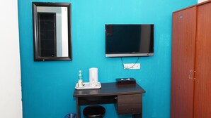 A room with a teal wall, a wooden wardrobe, a desk with a TV, a mirror, and a trash bin. - Hotel Shri Putiri (Pasir Gudang)