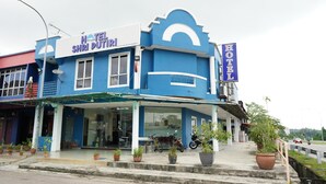 A hotel with a blue facade, a signboard with the hotel's name, and a covered entrance area with potted plants. - Hotel Shri Putiri (Pasir Gudang)