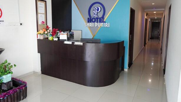 A hotel reception desk with a logo, a framed notice, and a potted plant. - Hotel Shri Putiri (Pasir Gudang)