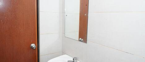 Um banheiro com porta de madeira, pia branca e espelho na parede.