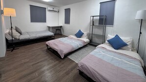 Une chambre avec deux lits simples, un bureau, une chaise et une étagère verticale.