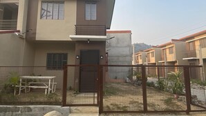 Un immeuble résidentiel moderne à deux étages, doté d’un toit plat, d’un balcon et d’une entrée sécurisée par un portail.