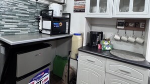 Une cuisine compacte avec des meubles blancs, un four à micro-ondes, une machine à café et un réfrigérateur.