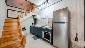 Una cocina moderna con refrigerador de acero inoxidable, escalera de madera y microondas.