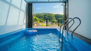 Una piscina interior pequeña con vistas a una colina boscosa.