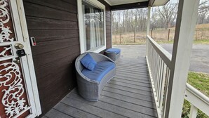 A covered porch with a dark wooden exterior, a white door with decorative glass panels, and a wicker sofa with blue cushions. - Private 10BR Secluded Compound, Spacious Retreat w/ Abundant Parking (Memphis)
