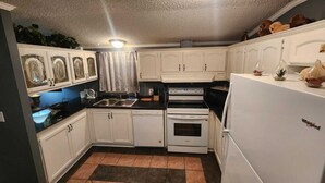A compact kitchen with white cabinets, a black countertop, a white refrigerator, and a tiled floor. - Private 10BR Secluded Compound, Spacious Retreat w/ Abundant Parking (Memphis)