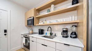 Une cuisine moderne avec des meubles blancs, un four à micro-ondes encastré, une machine à café et un mixeur.