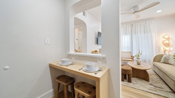 Une pièce moderne et bien éclairée, avec une table à manger en bois, deux tabourets, un canapé et une petite table ronde sur laquelle se trouve une lampe.