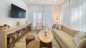 Un salon moderne avec un canapé, des tabourets en bois, une table basse et un téléviseur à écran plat fixé au mur.