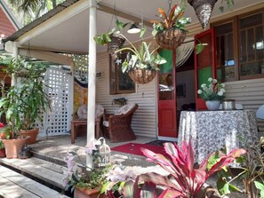 A covered porch with potted plants, wicker furniture, and a red door.