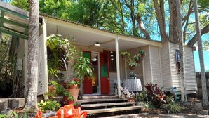 A house with a porch, steps leading to the entrance, and various potted plants. - Quirky Cottage in Centre of Maleny Walk Everywhere (Maleny)