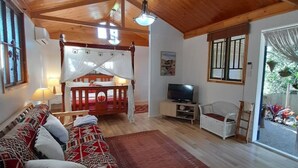A spacious room with a wooden ceiling, a bed with patterned bedding, a TV, a white chair, and a red rug. - Quirky Cottage in Centre of Maleny Walk Everywhere (Maleny)
