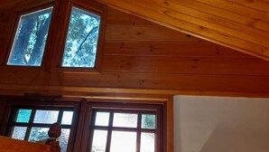 A wooden interior with a sloped ceiling, a large window with a view of trees, and a door with a view of a building. - Quirky Cottage in Centre of Maleny Walk Everywhere (Maleny)