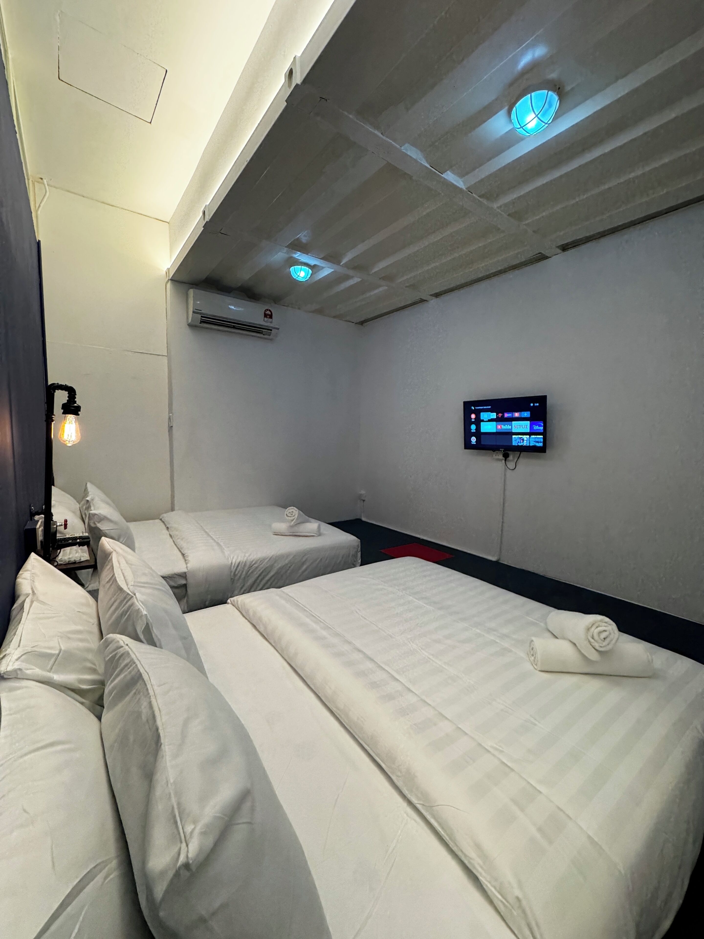 A hotel room with two beds, a flat-screen TV mounted on the wall, and a ceiling with recessed lighting.