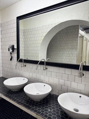 A bathroom with three white sinks, a large mirror, and a tiled wall. - The Harbour (George Town)