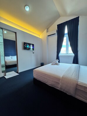A hotel room with a bed, a TV mounted on the wall, a window with curtains, and a ceiling light. - The Harbour (George Town)
