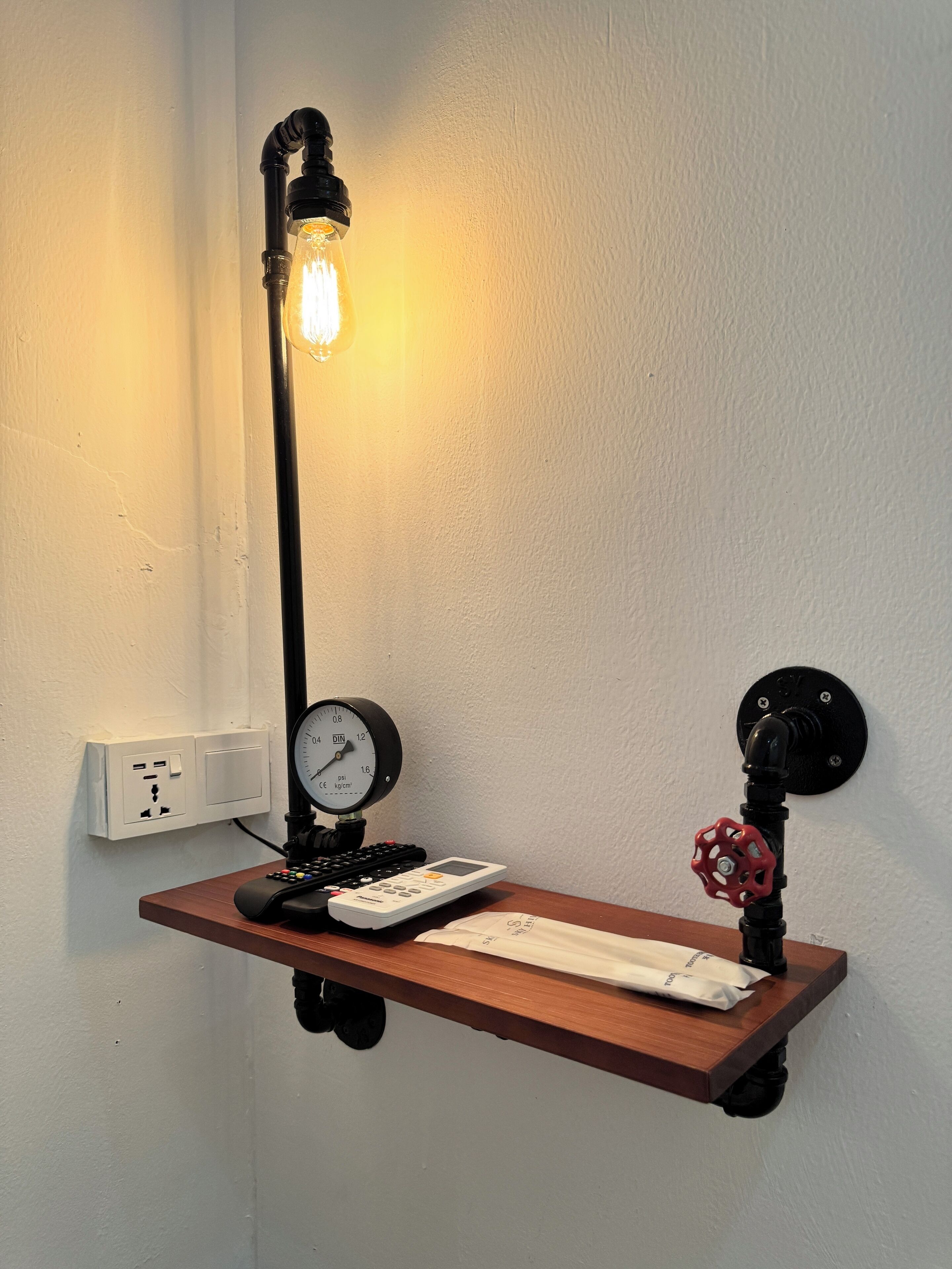 A wall-mounted shelf with a vintage-style lamp, a pressure gauge, and a red valve.