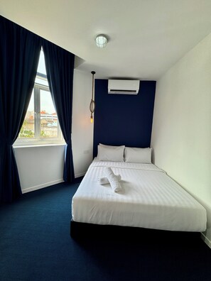 A hotel room with a large bed, dark blue curtains, a window with a view, and a ceiling light. - The Harbour (George Town)