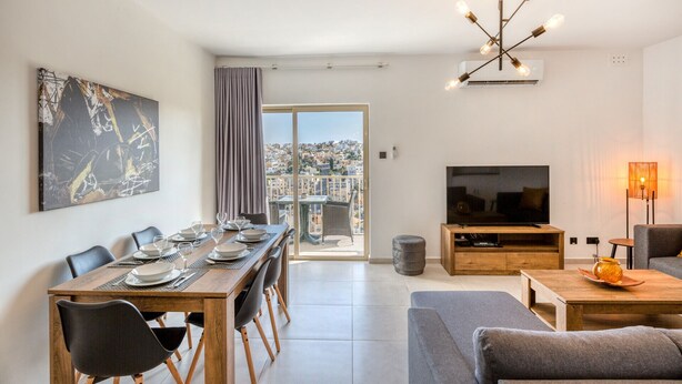 A modern living room with a dining area, a flat-screen TV, and a city view.
