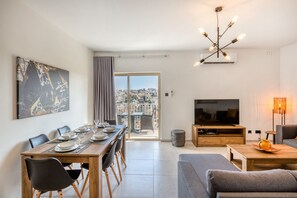 A modern living room with a dining area, a flat-screen TV, and a city view. - Amazing apartment with pool in Malta (Is-Swieqi)
