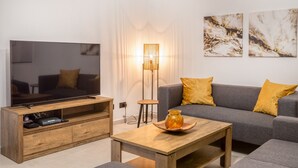 A modern living room with a flat-screen TV, wooden entertainment unit, a floor lamp, a sofa with yellow cushions, and abstract wall art.