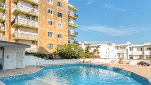 A swimming pool surrounded by a multi-story building with balconies and a clear sky.