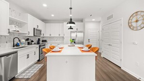 A modern kitchen with white cabinets, a central island, and an orange chair. - The Garden Luxe Retreat (Winter Garden)