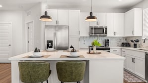 A modern kitchen with white cabinets, a stainless steel refrigerator, a microwave, and a central island with bar stools. - Winter Garden Charm, Near Disney (Winter Garden)