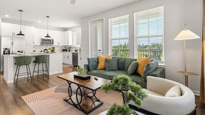 A modern kitchen with white cabinets, a central island, bar stools, and a dining area with a sofa and coffee table. - Winter Garden Charm, Near Disney (Winter Garden)