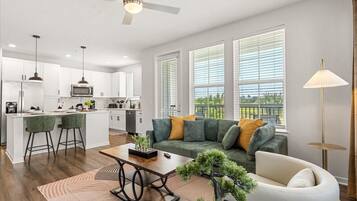 A modern kitchen with white cabinets, a central island, bar stools, and a dining area with a sofa and coffee table.