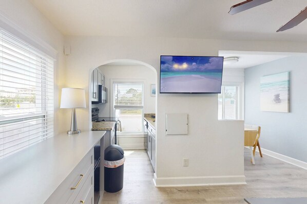Una cocina moderna con un televisor grande, un cubo de basura y una zona de comedor con una mesa y sillas.