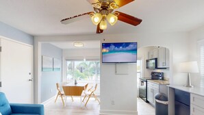 A modern kitchen with a TV, a ceiling fan, and a dining area with a table and chairs. - Upper Level Retreat, Courtyard, Walk to Beach & John’s Pass +Tickets Included to Top Attractions. (Treasure Island)