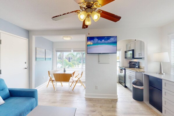 A modern kitchen with a TV, a ceiling fan, and a dining area with a table and chairs. - Upper Level Retreat, Courtyard, Walk to Beach & John’s Pass +Tickets Included to Top Attractions. (Treasure Island)