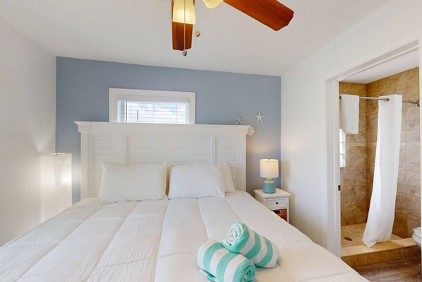 A bedroom with a large bed, a nightstand, a lamp, and a view of a bathroom with a shower. - Upper Level Retreat, Courtyard, Walk to Beach & John’s Pass +Tickets Included to Top Attractions. (Treasure Island)