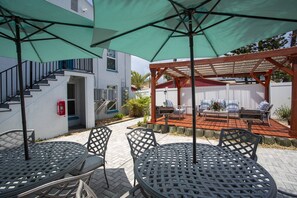 A patio area with outdoor seating, including round tables and chairs, under green umbrellas. - Upper Level Retreat, Courtyard, Walk to Beach & John’s Pass +Tickets Included to Top Attractions. (Treasure Island)