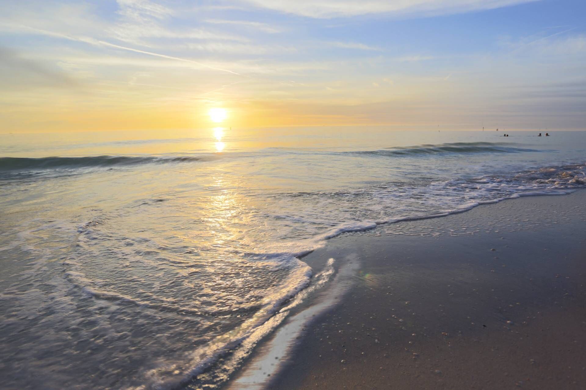 A beach with waves gently lapping at the shore under a clear sky.