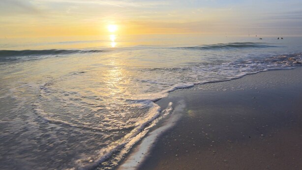 A beach with waves gently lapping at the shore under a clear sky.