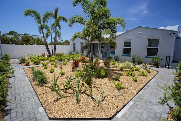 A landscaped garden area with various plants and a paved walkway. - Upper Level Retreat, Courtyard, Walk to Beach & John’s Pass +Tickets Included to Top Attractions. (Treasure Island)