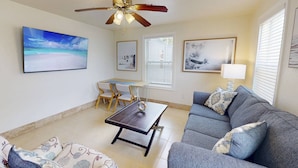A living room with a ceiling fan, a dining table with chairs, a sofa, and artwork on the walls.
