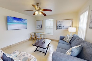 A living room with a ceiling fan, a dining table with chairs, a sofa, and artwork on the walls.
