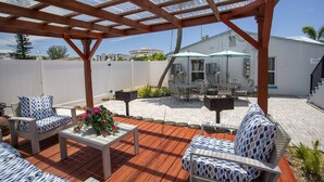A covered patio area with outdoor furniture, a table with a flower centerpiece, and a white building in the background.