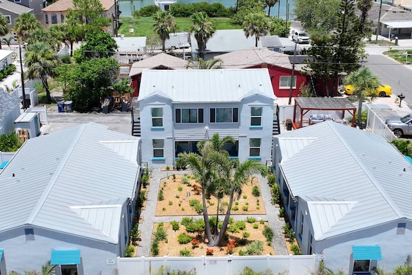 A two-story building with a central courtyard featuring palm trees and small plants. - Charming “Coral” 1BR Steps from Beach, Walk to John’s Pass, King Bed, + Tickets to Fun Activities! (Treasure Island)