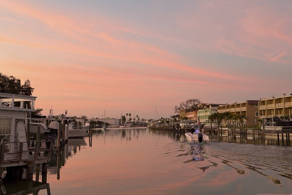 A marina with boats docked, a calm water surface, and buildings in the background.