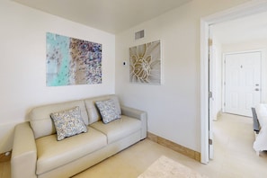 Un salon avec un canapé beige, deux coussins à motifs et deux œuvres d’art accrochées au mur.