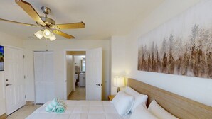 A hotel room with a bed, a ceiling fan, a painting, and a bathroom visible through an open door.