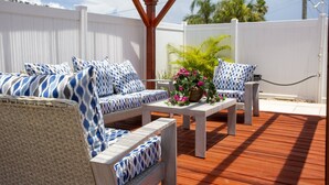 An outdoor patio with wicker furniture, a white fence, and a wooden pergola.
